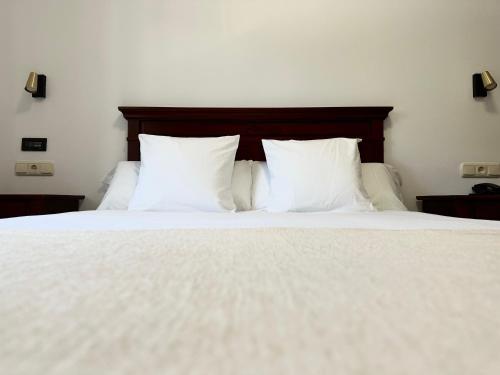 uma cama com lençóis brancos e almofadas em Hostal La Muralla em Zahara de los Atunes