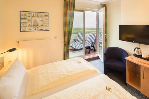 a hotel room with a bed and a television and a balcony at Hotel Strandburg in Baltrum