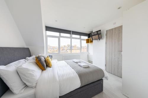 a white bedroom with a large bed with a window at Cozy Rooms with Shared Kitchen and Laundry Area in London