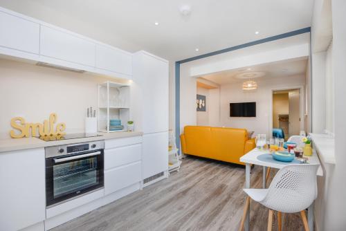 a kitchen with white cabinets and a table and a yellow couch at Apartment One - Private Car Park - King Bed - by Ocean City Retreats in Plymouth