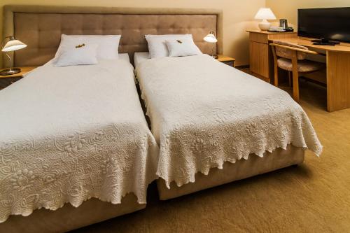 two beds in a room with a desk and a television at Hotel Komeda in Ostrów Wielkopolski