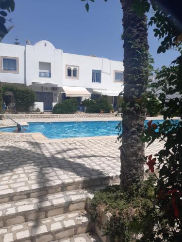 a palm tree in front of a building with a swimming pool at Résidence meriem 2 in Hammamet