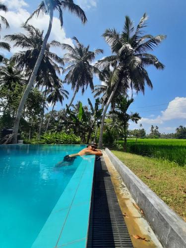 a person laying on the edge of a swimming pool with palm trees at Rice Rice Villas in Tissamaharama