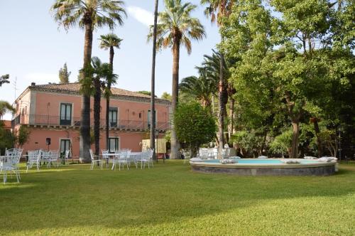 un prato con sedie, un edificio e palme di Le stanze dei Mori - quadrupla con bagno privato a Mascalucia