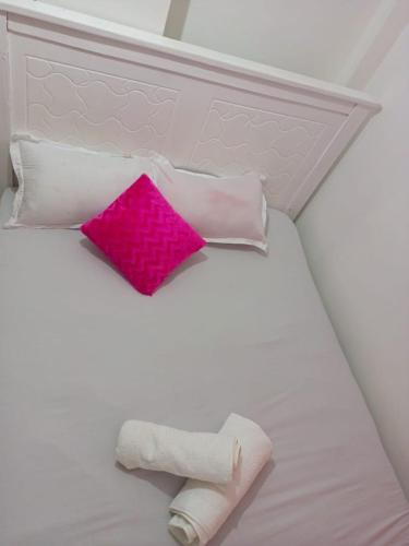een wit bed met een roze kussen en kussens bij Triad apartments in Nairobi