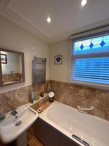 ein Bad mit einem Waschbecken, einer Badewanne und einem Fenster in der Unterkunft Toosey Lass - St Osyth creek in Saint Osyth