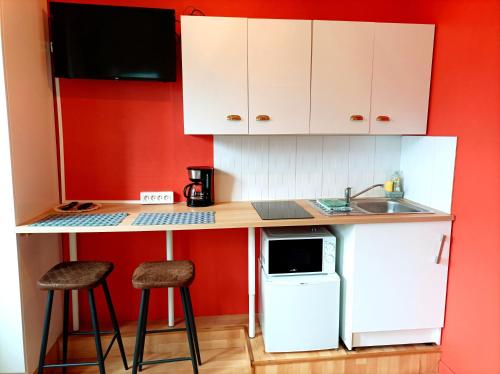 Le studio Naturel في هينان بومونت: مطبخ صغير بجدران حمراء ودواليب بيضاء