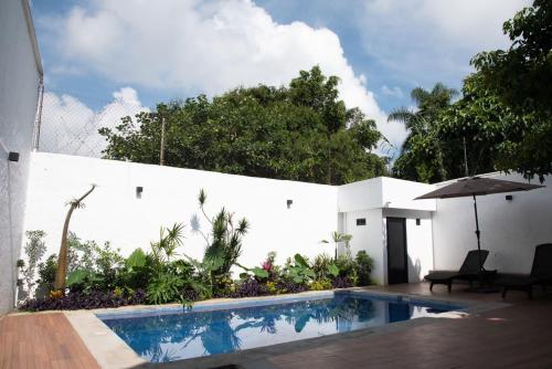 a swimming pool with an umbrella next to a white wall at Casa Naâmja in Tepoztlán