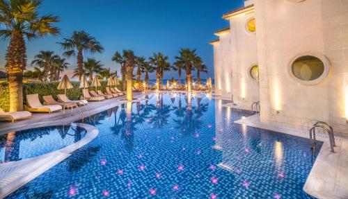 a pool at a resort with chairs and palm trees at Palazetto Suites Zakynthos - Adults Only in Tsilivi