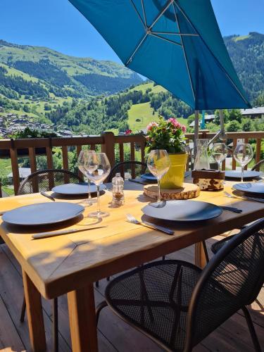 a wooden table with wine glasses and a blue umbrella at Appartement haut standing Arêches beaufort in Arêches