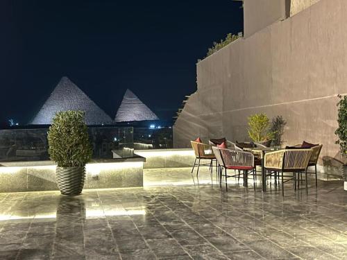 um pátio com cadeiras e uma mesa com pirâmides ao fundo em Pyramid Front Hotel no Cairo