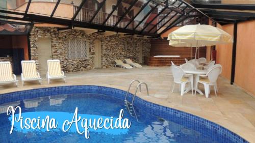 a pool with a table and chairs and an umbrella at Hotel Monte Carlo in Campos do Jordão
