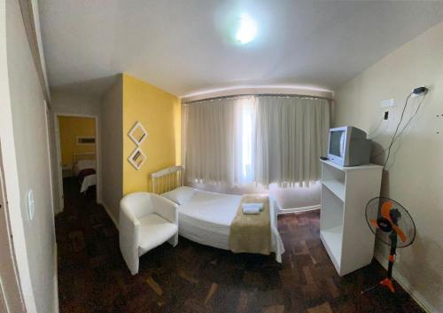 a bedroom with a white bed and a tv at Hotel Domo in Prudentópolis