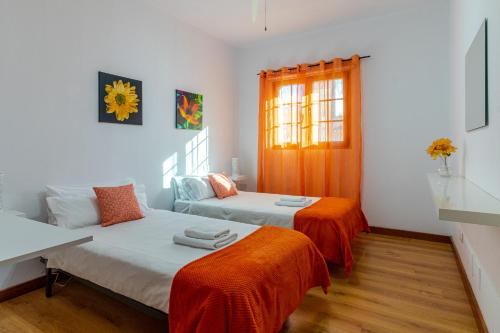 1 dormitorio con 2 camas con sábanas de color naranja y ventana en Villa de Pino, en Firgas
