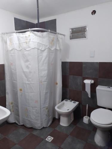 a bathroom with a toilet and a white shower curtain at Veredas al sol puerto piramides in Puerto Pirámides