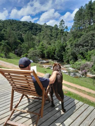 a man sitting in a chair with a dog at Morada Vale das Águas in São Bonifácio