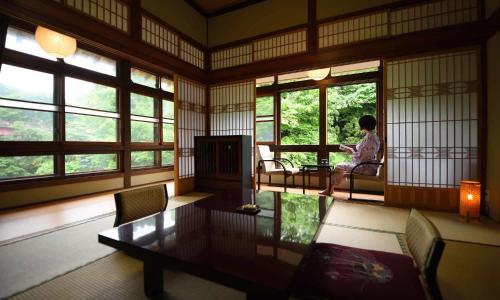 a woman sitting in a room with a table and windows at Fujisan Ryokan in Hanamaki
