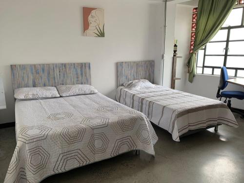a bedroom with two beds and a chair and windows at La Curva Apartamentos in Cali