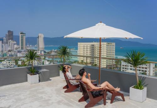 two women sitting in chairs on a balcony with an umbrella at Hotel Soco in Da Nang