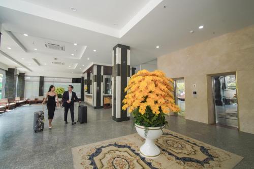 a man and woman walking through a lobby with a vase of flowers at Hotel Soco in Da Nang