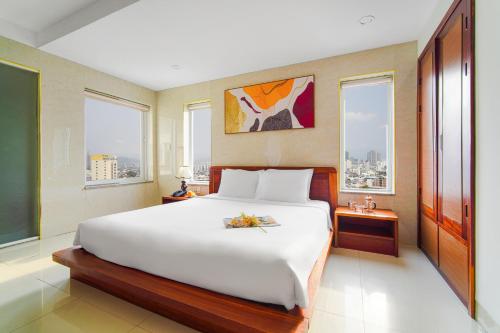 a bedroom with a large white bed with windows at Hotel Soco in Da Nang