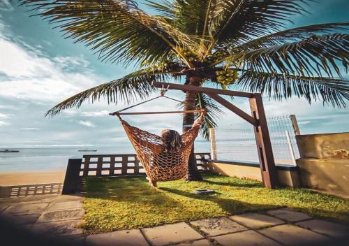 a person laying in a hammock under a palm tree at Pousada La Riviera in Maragogi