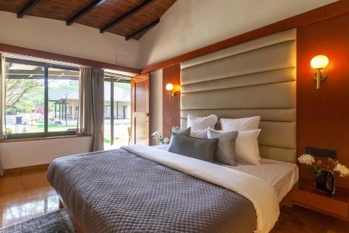 een slaapkamer met een groot bed en een groot raam bij StayVista's Lush Villa - Lake-View Haven with Rustic-Meets-Modern Interiors, Pool, Jacuzzi & Indoor activities in Wādhiware
