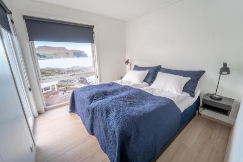 um quarto com uma cama com um cobertor azul e uma janela em Runde Panorama - Trollvogga em Runde