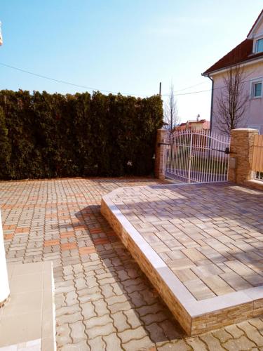a brick driveway with a stone bench in front of a fence at Valloris Apartments in Hévíz