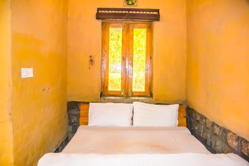 a bed with two pillows in a room with a window at Prakriti Aalay - Riverside Mountain View Boutique Eco Resort in Dharamshala