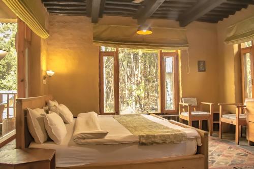 a bedroom with a bed in a room with windows at Prakriti Aalay - Riverside Mountain View Boutique Eco Resort in Dharamshala
