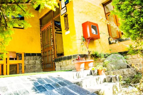 a yellow building with potted plants in front of it at Prakriti Aalay - Riverside Mountain View Boutique Eco Resort in Dharamshala