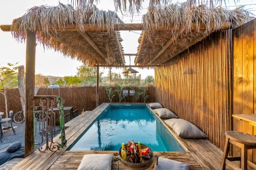 a swimming pool with a straw roof and a wooden deck at הבית החום בערבה in Sappir