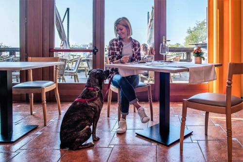 a woman sitting at a table with a dog at Hotel Caneo in Fossalòn