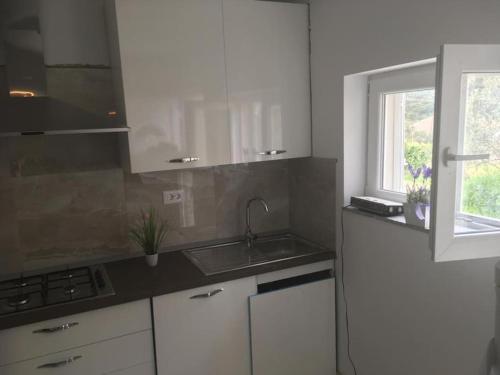 a kitchen with white cabinets and a sink and a window at Apartman Milica in Vrgada