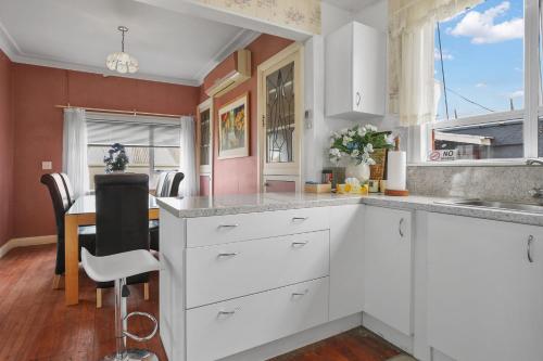 a kitchen with white cabinets and a dining table at Terracotta Cottage in Te Awamutu