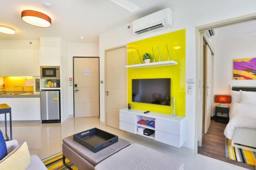 a living room with a yellow accent wall and a television at Cassia Phuket, part of Banyan Group in Bang Tao Beach