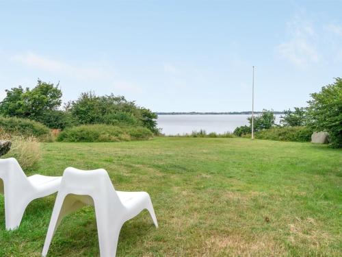 duas cadeiras brancas sentadas num campo ao lado de uma massa de água em Holiday Home Sissela - 5m from the sea in Funen by Interhome em Ebberup