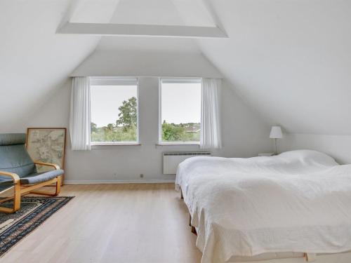 a bedroom with a bed and a chair and two windows at Holiday Home Sissela - 5m from the sea by Interhome in Ebberup
