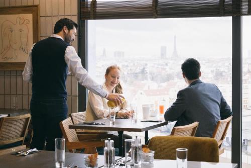 a man serving a woman at a table in a restaurant at KOPSTER Hotel Residence Paris Ouest Colombes in Colombes