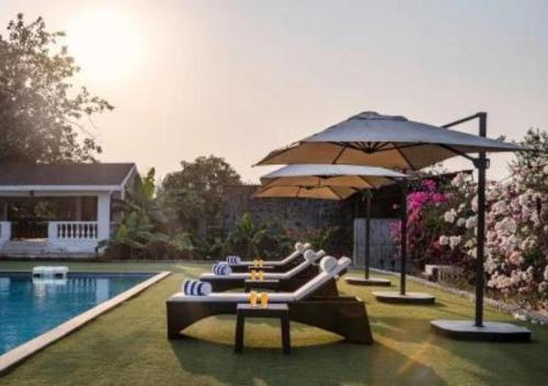 a pool with several lounge chairs and an umbrella at SaffronStays Brunton House, Alibaug - luxury pool villa near Awas Beach in Alibaug