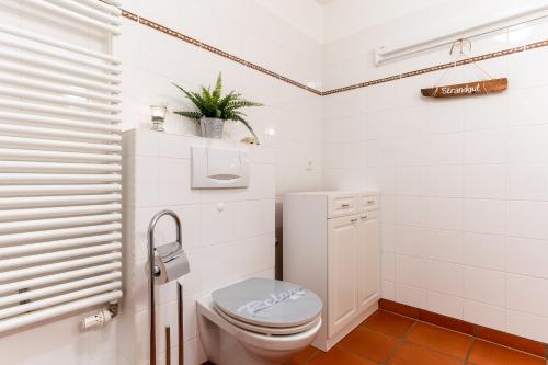 a white bathroom with a toilet and a plant at Appartementhaus Appartement Strandläufer in Süderhöft