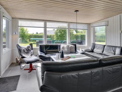 ein Wohnzimmer mit einem schwarzen Ledersofa und Stühlen in der Unterkunft Holiday Home Edel - 650m from the sea in NE Jutland by Interhome in Hadsund