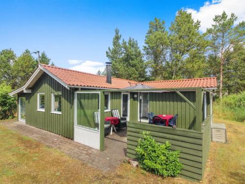 a green cabin with a deck with two chairs at Holiday Home Elmer - 400m from the sea in NE Jutland by Interhome in Jerup