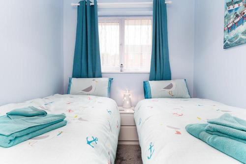 two twin beds in a bedroom with blue curtains at Pebbles Reach in Llanddulas