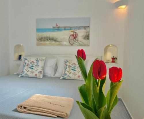 Habitación con cama con jarrón de flores rojas en La Dimora 4: Charm and Quiet, en SantʼAgata sui Due Golfi