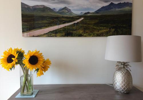 a vase with sunflowers on a table next to a painting at The Roses B&B in Portree