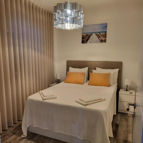 a bedroom with a large white bed and a chandelier at Nandos Apartement in Costa da Caparica