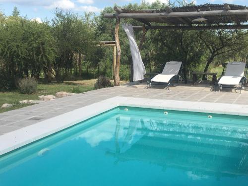 a swimming pool with two chairs and a pergola at Color Local Cabañas in San Javier