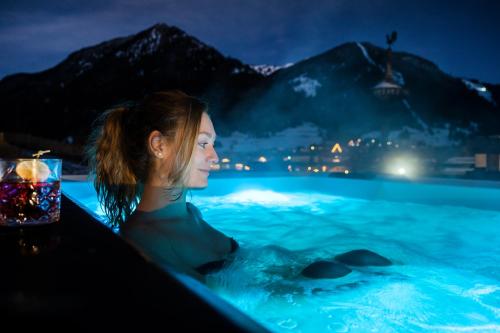 a woman sitting in a swimming pool at night at Ladinia Dolomites View - Adults Only in Pozza di Fassa